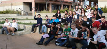 students seated outdoors on tiered steps. Waving at camera.